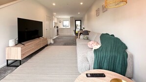 Een moderne woonkamer met een flatscreen televisie, een bank, een salontafel en een eethoek op de achtergrond.