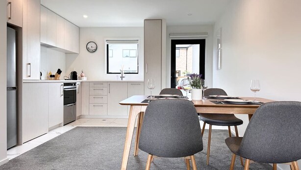 Een moderne keuken met inbouwapparatuur, een eethoek met een tafel en stoelen, en uitzicht buiten door een raam.