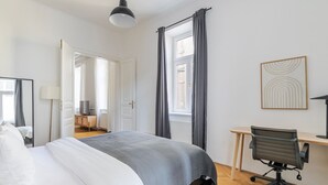 A hotel room with a bed, a desk, a chair, a lamp, and a window with curtains. - Blueground | Josefstadt, washer/dryer, nr Votivkirche (Vienna)