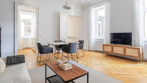 A modern living room with a dining area, a TV on a wooden cabinet, and a large window with curtains. - Blueground | Josefstadt, washer/dryer, nr Votivkirche (Vienna)