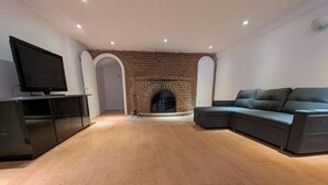 A spacious living room with a brick fireplace, a large sectional sofa, and a flat-screen TV on a stand. - Home rental S7 (Bois-des-Filion)
