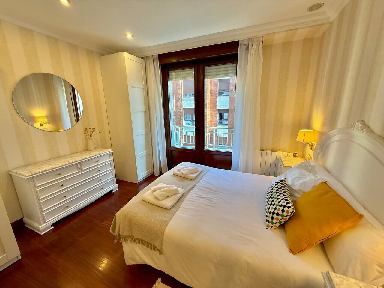 A hotel room with a large bed, a dresser, a mirror, and a view of the outside.