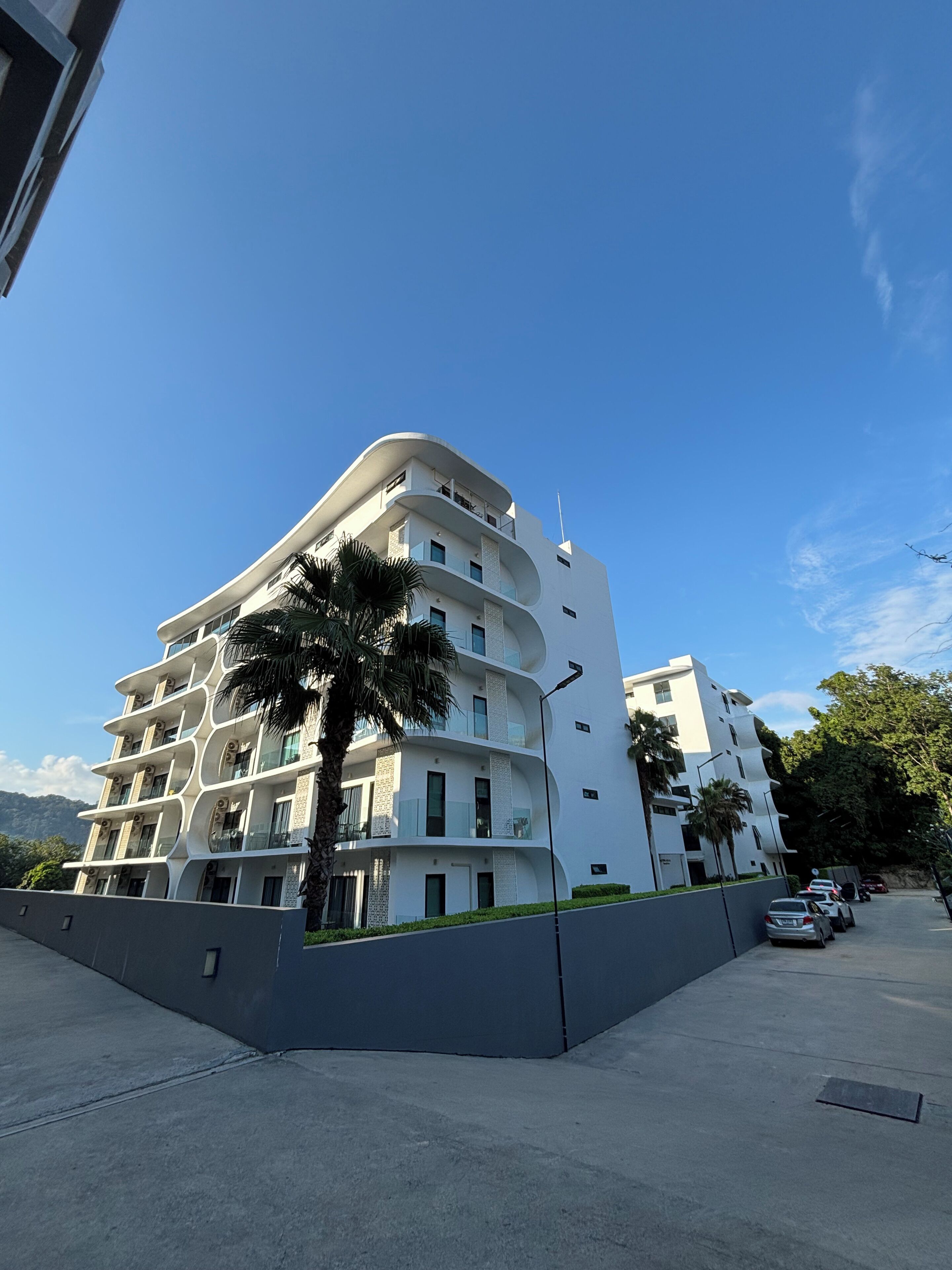 A multi-story hotel with balconies, palm trees, and a clear blue sky.