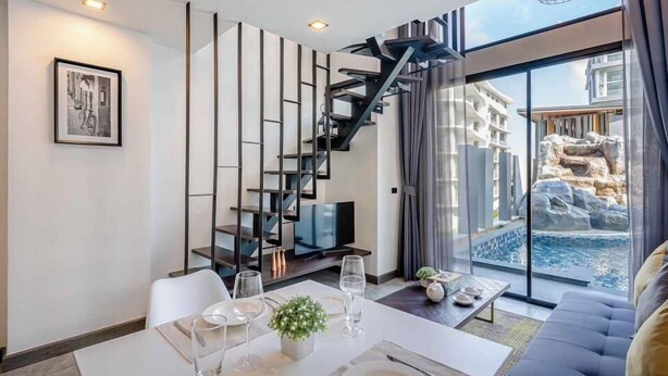 A modern living room with a staircase, a dining area, and a large window offering a view of a rocky landscape. - Utopia Loft Aparthotel by Sabai Sands (Rawai)