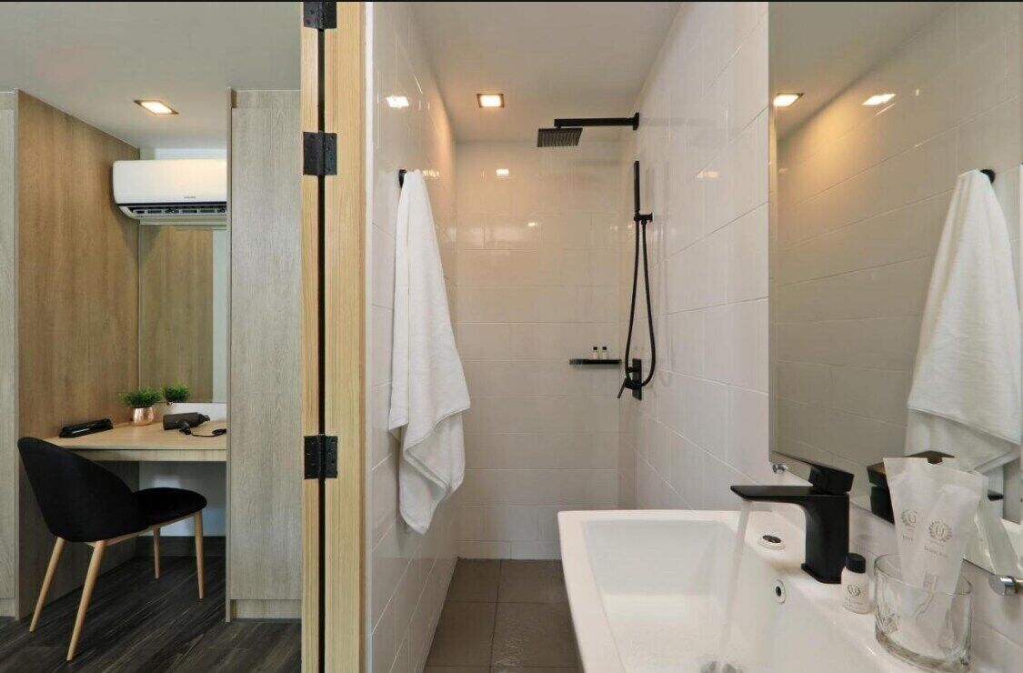 Une salle de bain moderne équipée d’une douche, d’une baignoire et de toilettes. On y trouve un bureau avec une chaise et une petite plante.