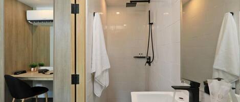 Une salle de bain moderne équipée d’une douche, d’une baignoire et de toilettes. On y trouve un bureau avec une chaise et une petite plante.