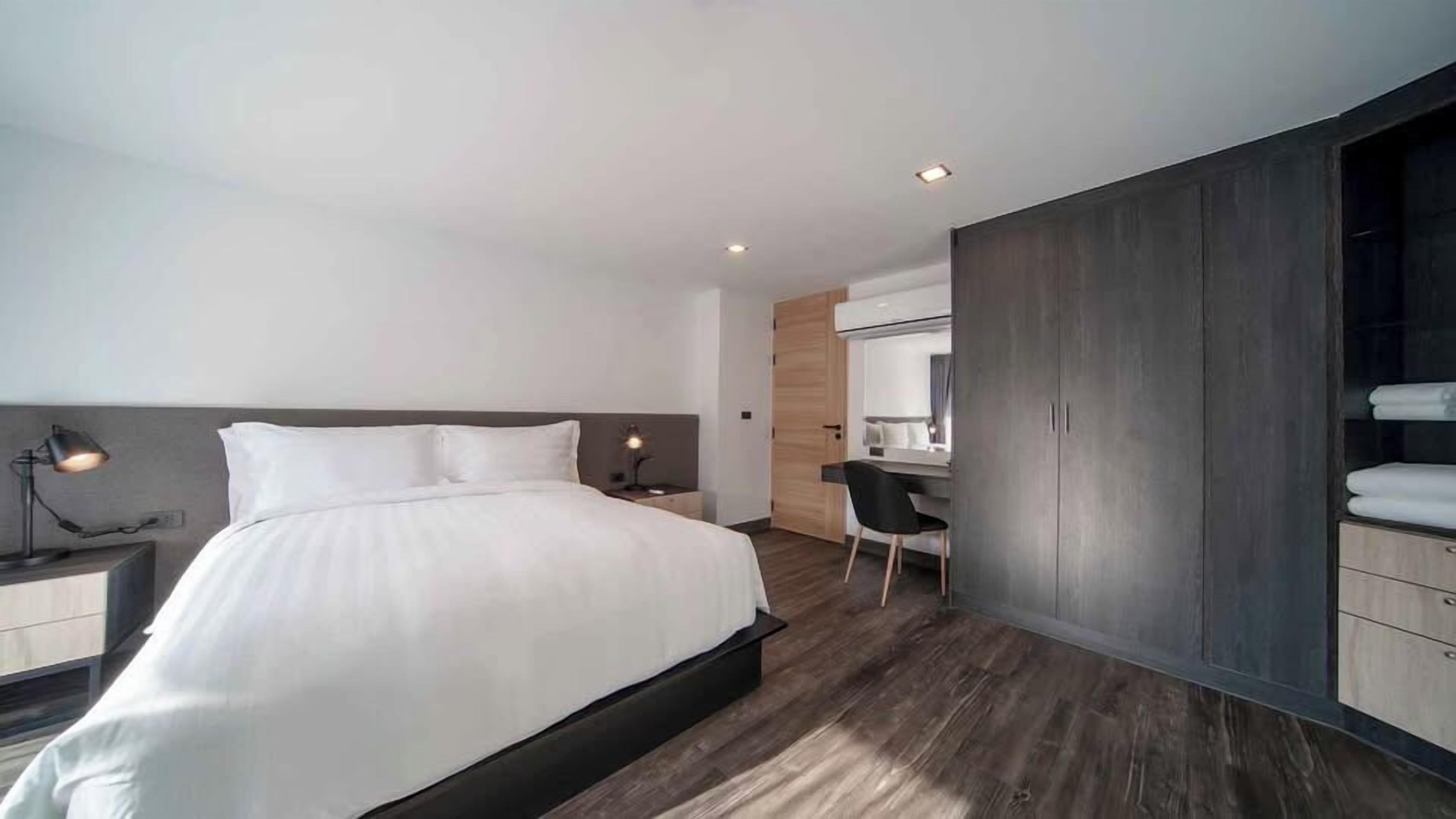 A modern bedroom with a large bed, bedside lamps, a desk, and a wardrobe.