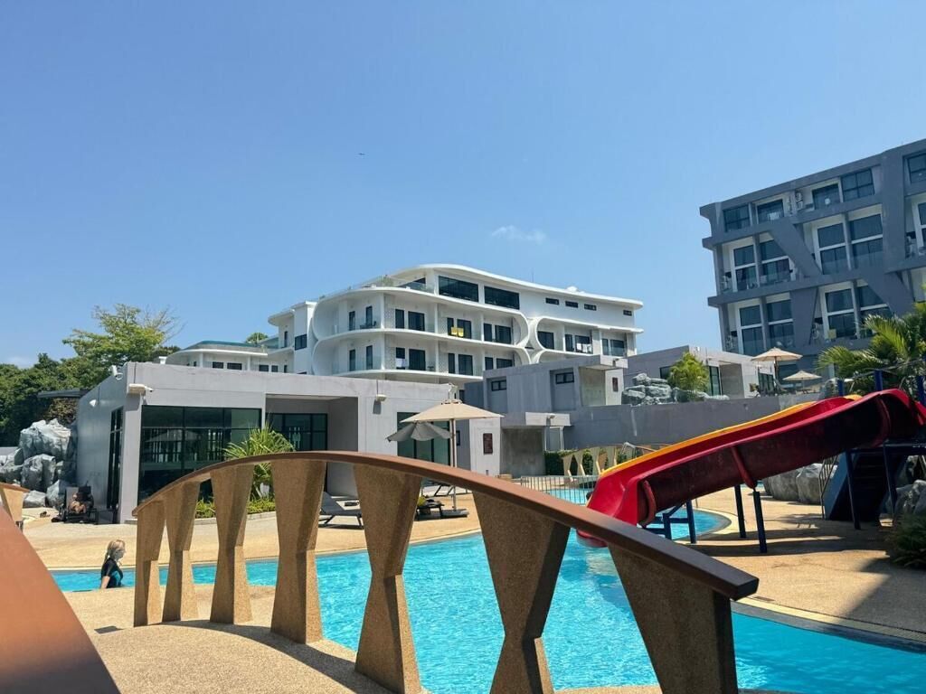 A swimming pool area with a modern building in the background, a slide, and a clear blue sky.