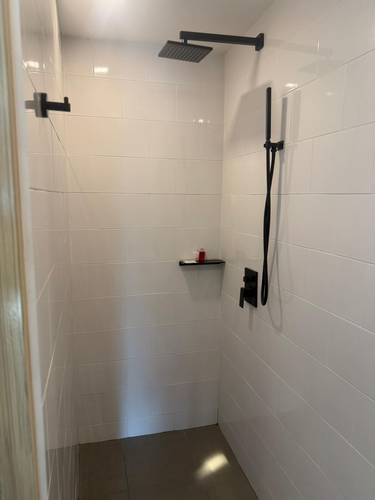 A small, tiled shower room with a handheld showerhead and a wall-mounted faucet.
