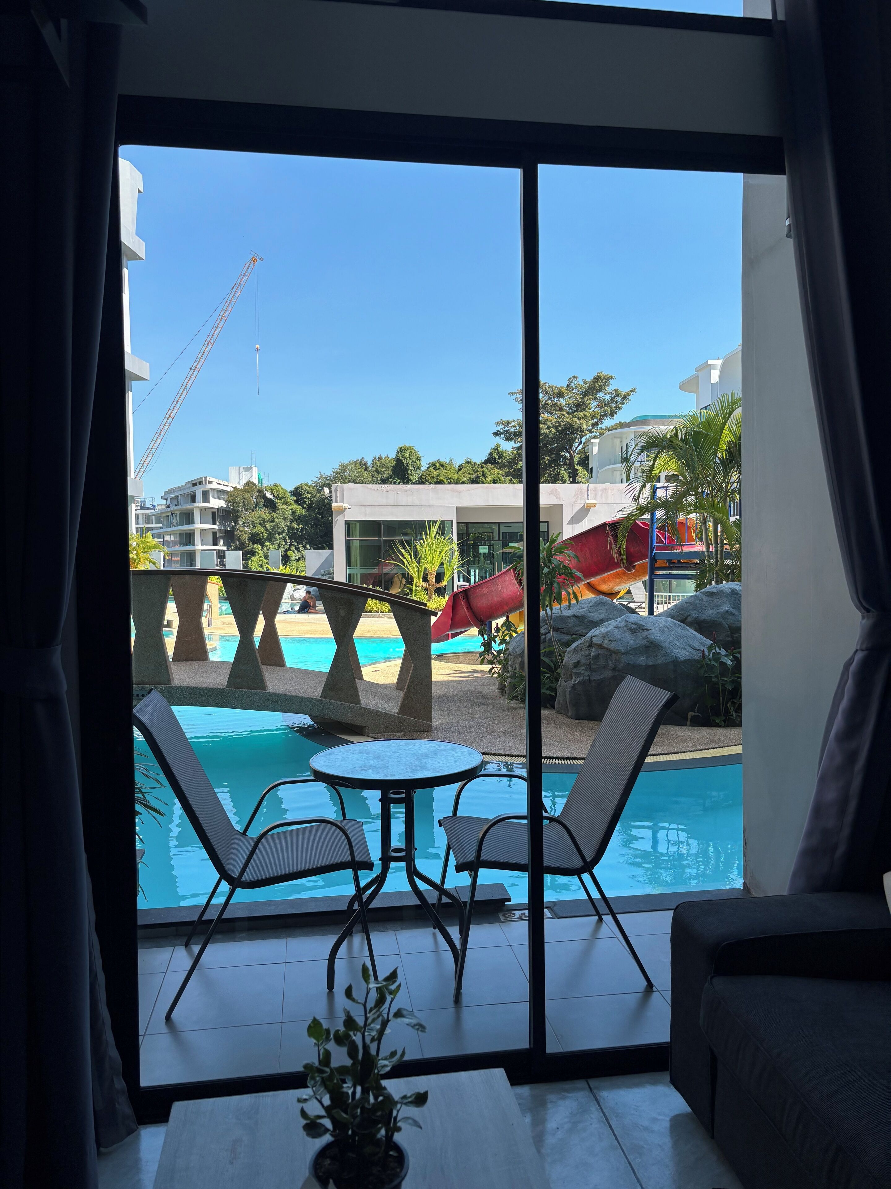 A room with a large sliding glass door leading to a pool area, featuring a table and chairs, and a potted plant.