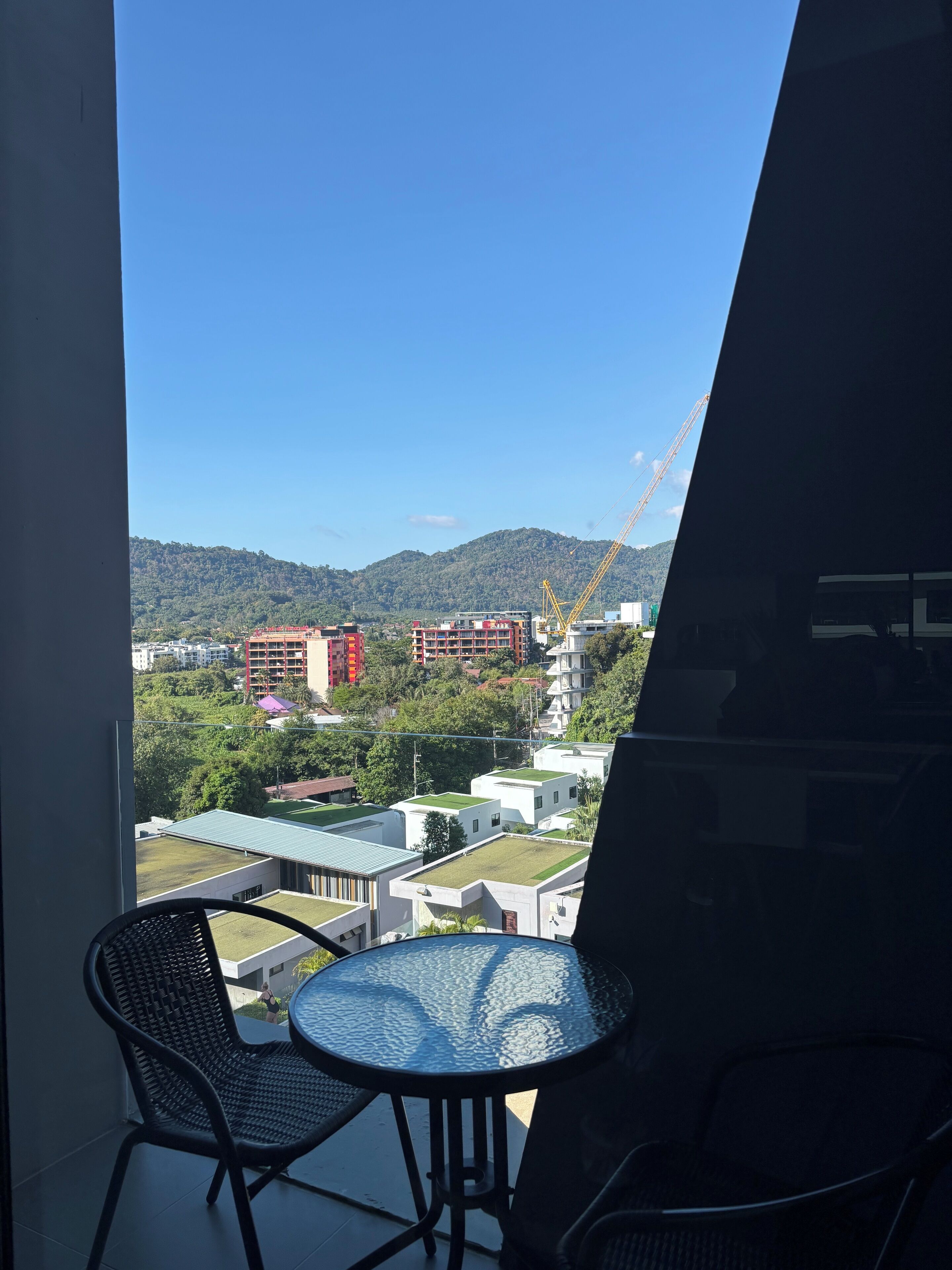A balcony with a table and chairs, overlooking a cityscape with buildings and a construction crane.