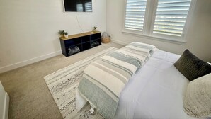 Una camera da letto con un letto, una TV a muro, un mobile contenitore in legno e due finestre con persiane.