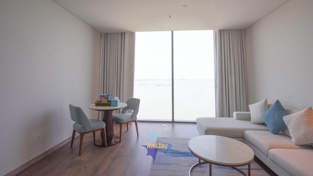 A modern living room with a sofa, chairs, a coffee table, and a view of the sea through large windows. - OceanView Hạ Long • Large Balcony • TwinBed (Thành phố Hạ Long)