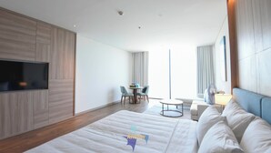 A modern hotel room with a large bed, a flat-screen TV mounted on the wall, a small round table with chairs, and a window with curtains. - OceanView Hạ Long • Large Balcony • TwinBed (Thành phố Hạ Long)