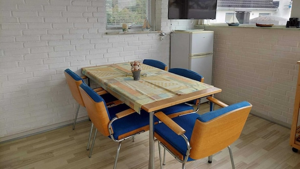 Un comedor con mesa, sillas, televisor y refrigerador.