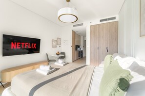 A modern hotel room with a large bed, a television mounted on the wall, a small dining area, and a kitchenette in the background. - Peninsula One - 1312 Studio (Dubai)