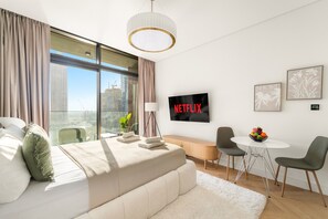 A modern hotel room with a large bed, a TV, a desk with chairs, and a view of the city. - Peninsula One - 1312 Studio (Dubai)