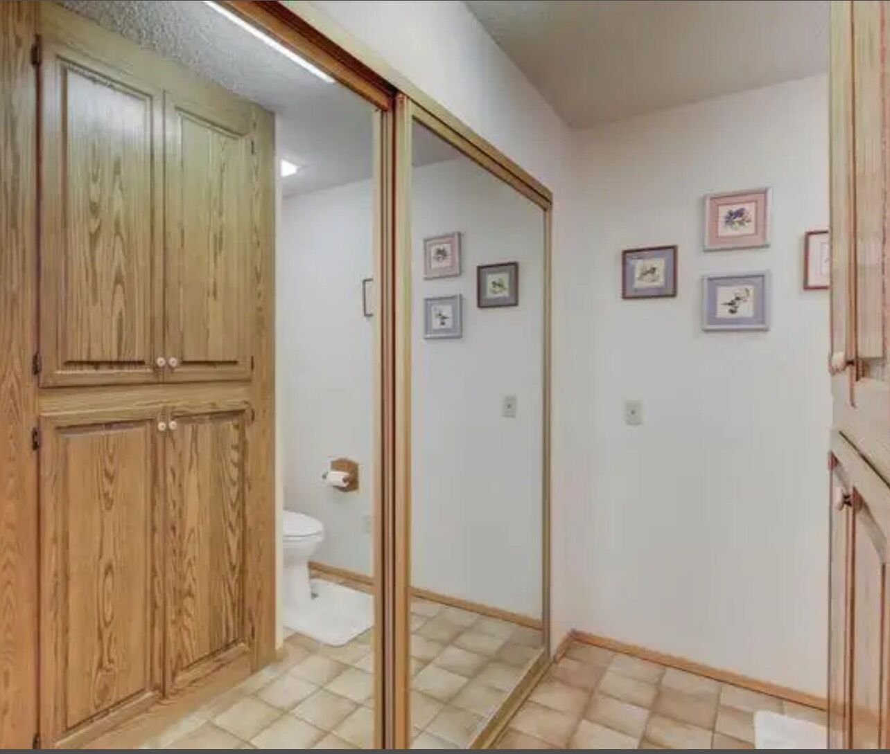 Une salle de bain avec des meubles en bois, des toilettes et des tableaux encadrés accrochés au mur.