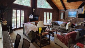 A cozy cabin interior with a wooden ceiling, large windows, a television, and a fireplace. - Charming 3-bedroom country house with AC in Shingletown (Shingletown)