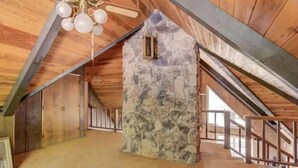 An attic room with a sloped ceiling, exposed wooden beams, and a stone wall. - Charming 3-bedroom country house with AC in Shingletown (Shingletown)