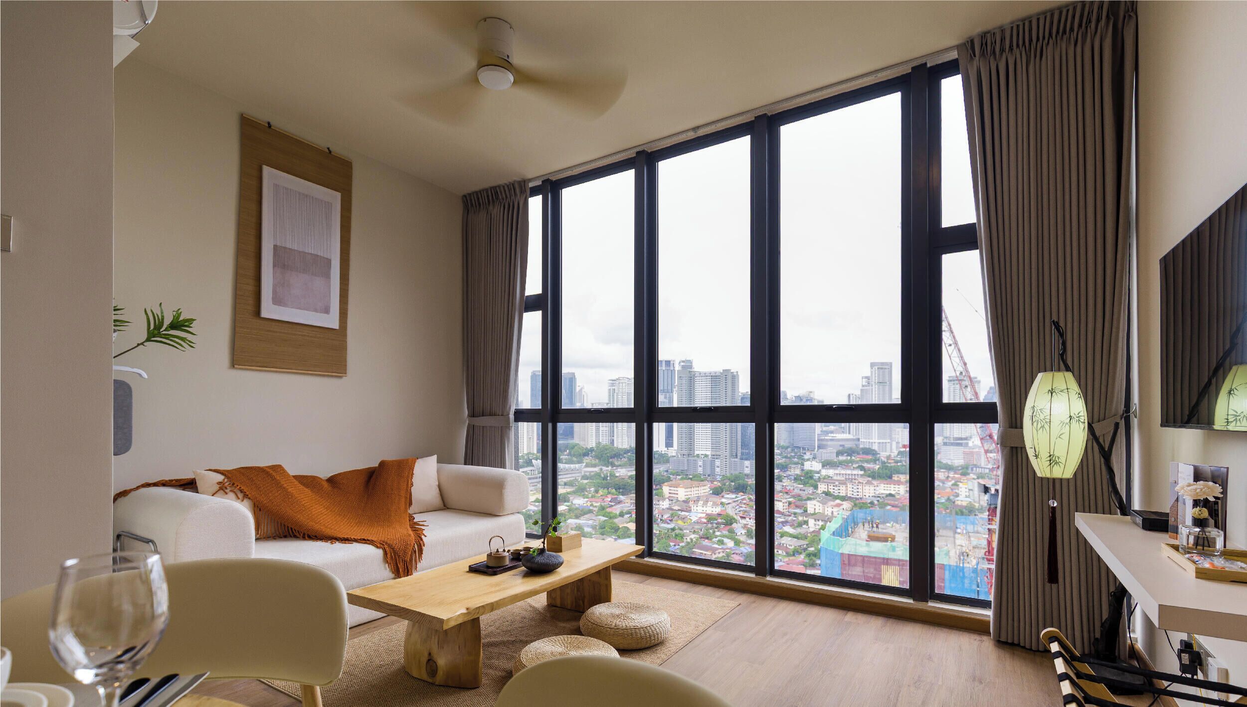 A modern living room with a large window, a sofa, a coffee table, and a view of a cityscape.