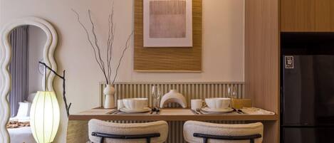 A dining area with a wooden table, two chairs, a vase with branches, and a modern light fixture.