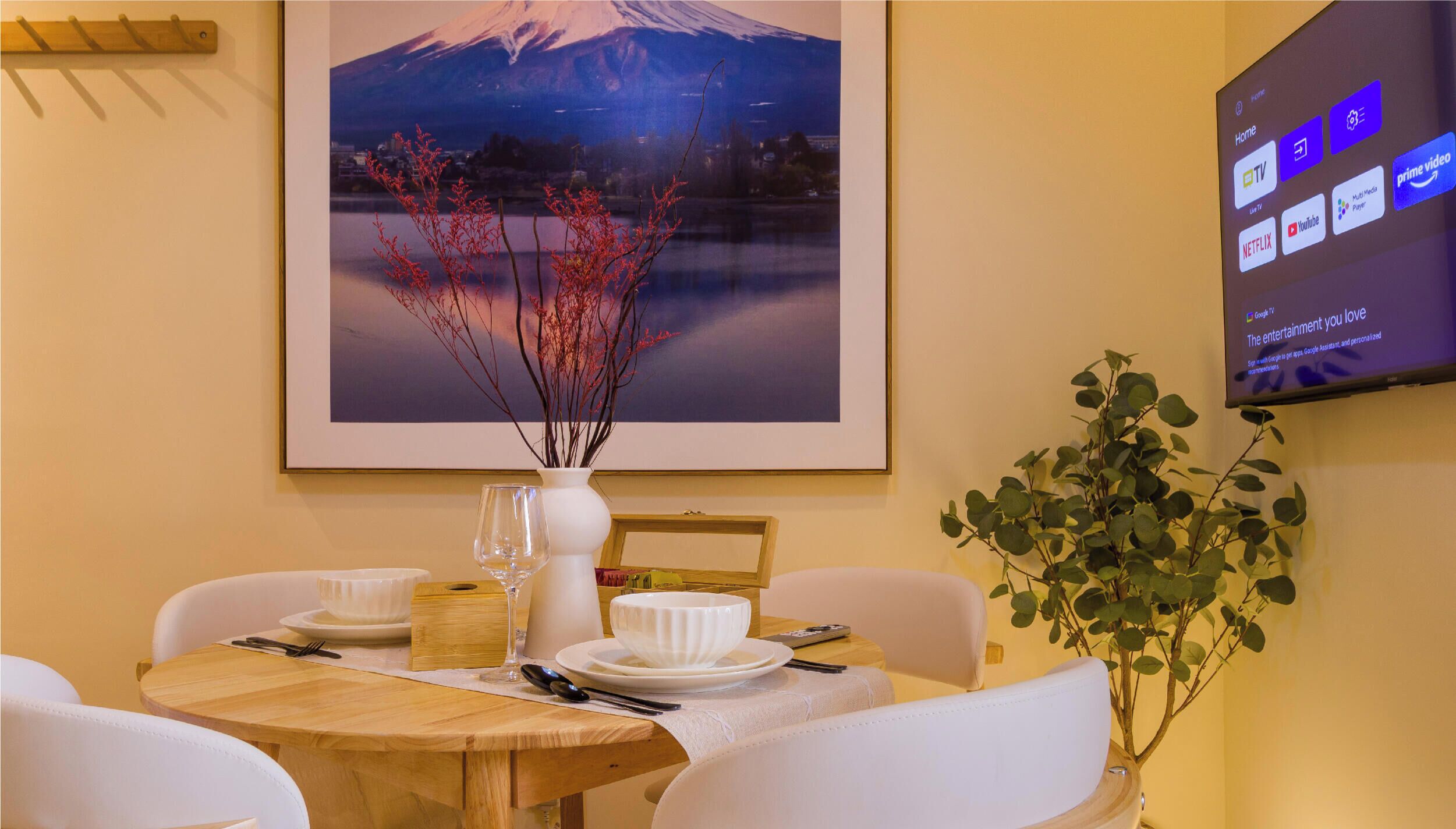 A dining area with a table set for two, a framed picture of a mountain, and a television displaying streaming services.