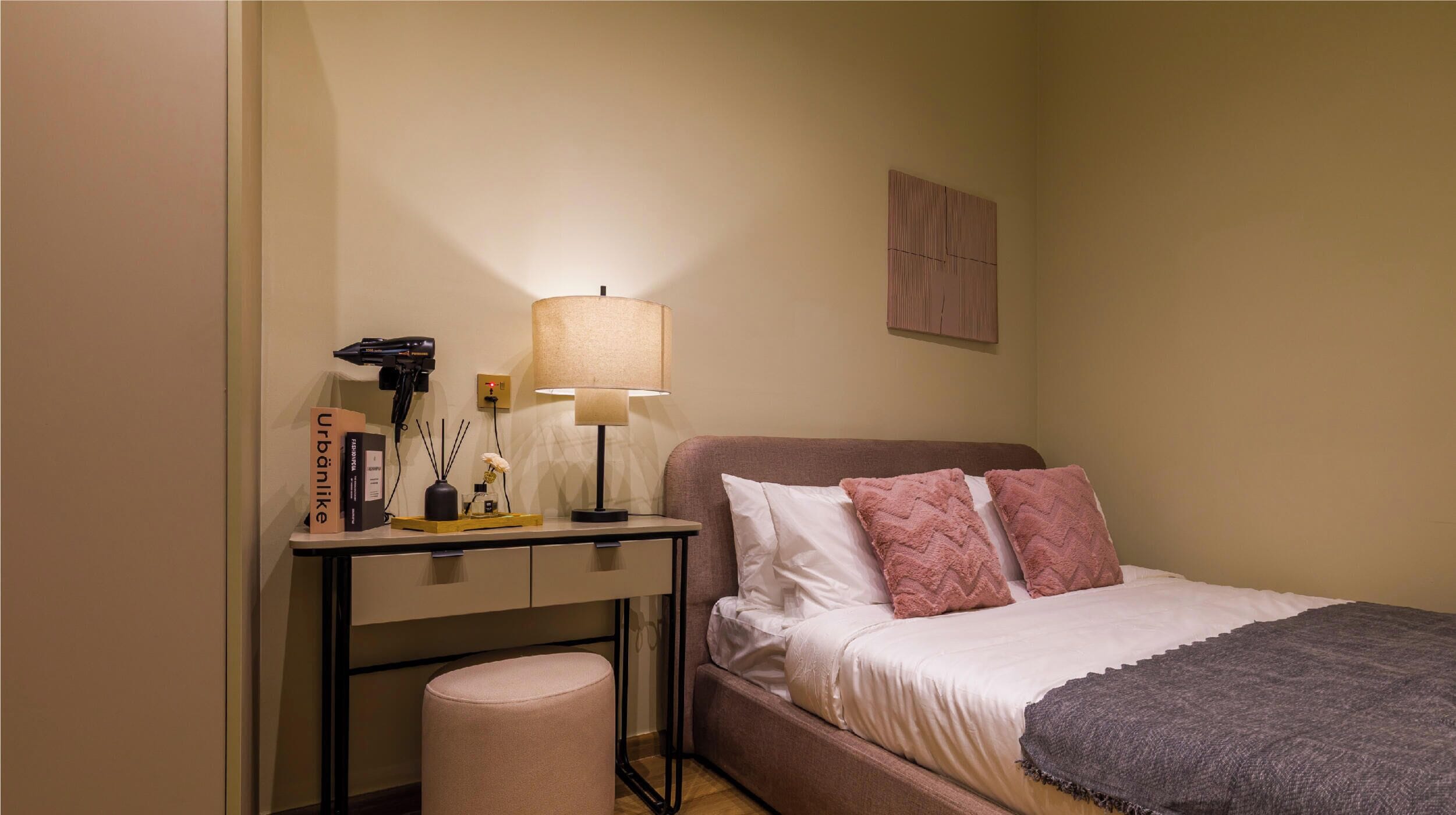 Een slaapkamer met een bed, nachtkastje, lamp en een klein krukje.