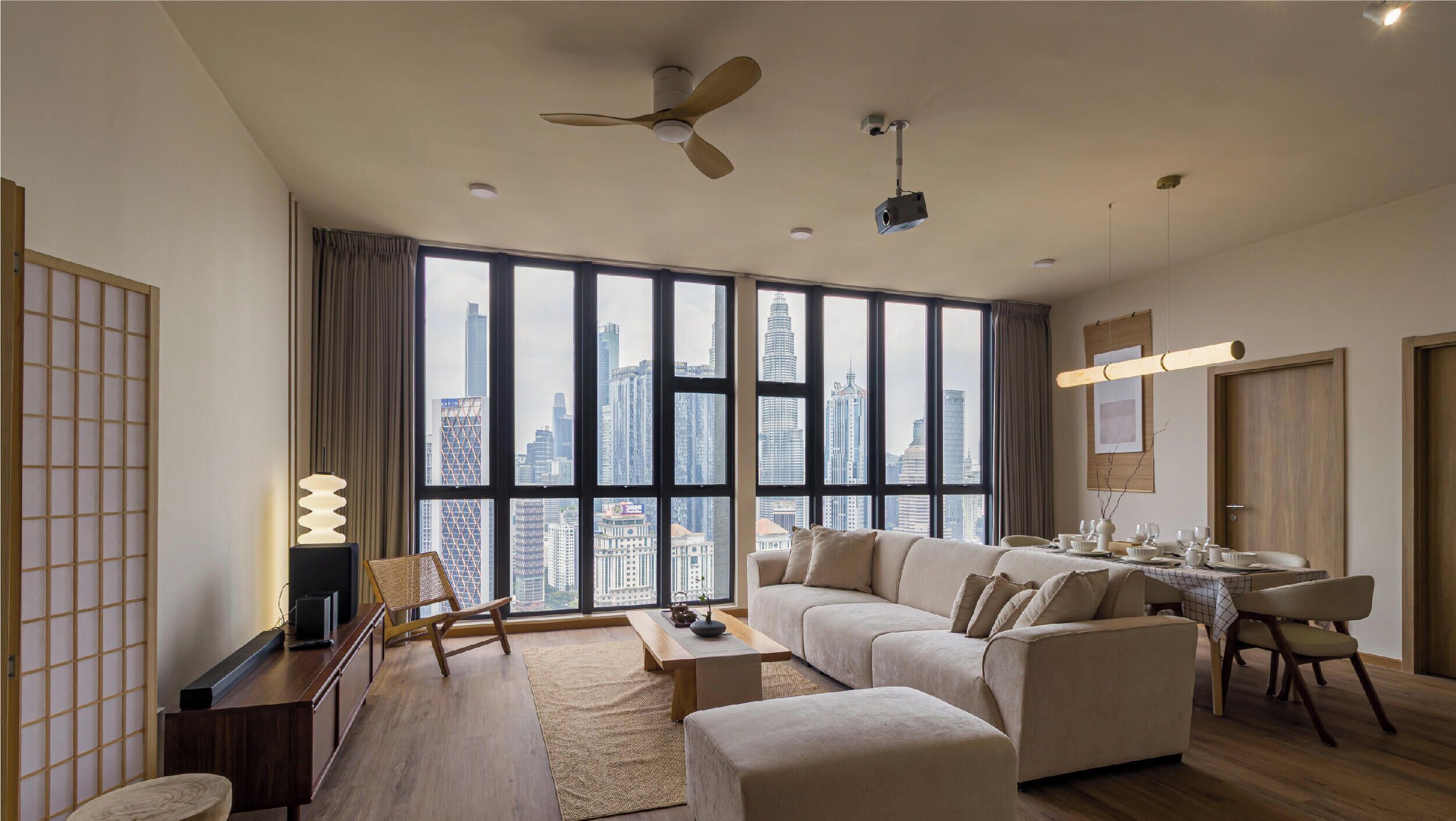 A modern living room with a sofa set, a dining table, and a view of the cityscape through large windows.