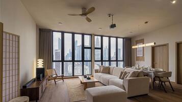 A modern living room with a sofa set, a dining table, and a view of the cityscape through large windows.