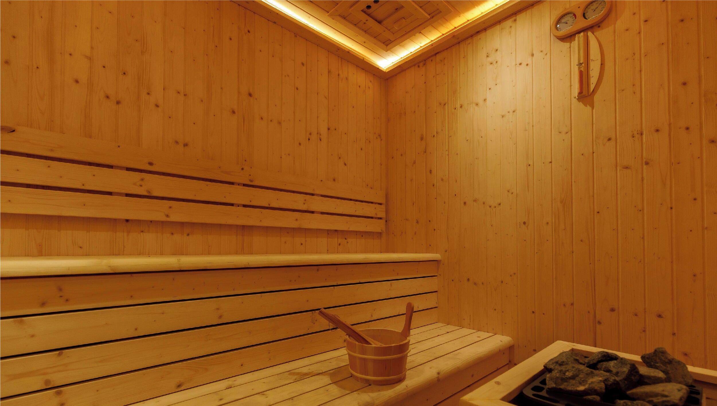 Una sauna de madera con bancos, un balde de madera y un banco de piedra.