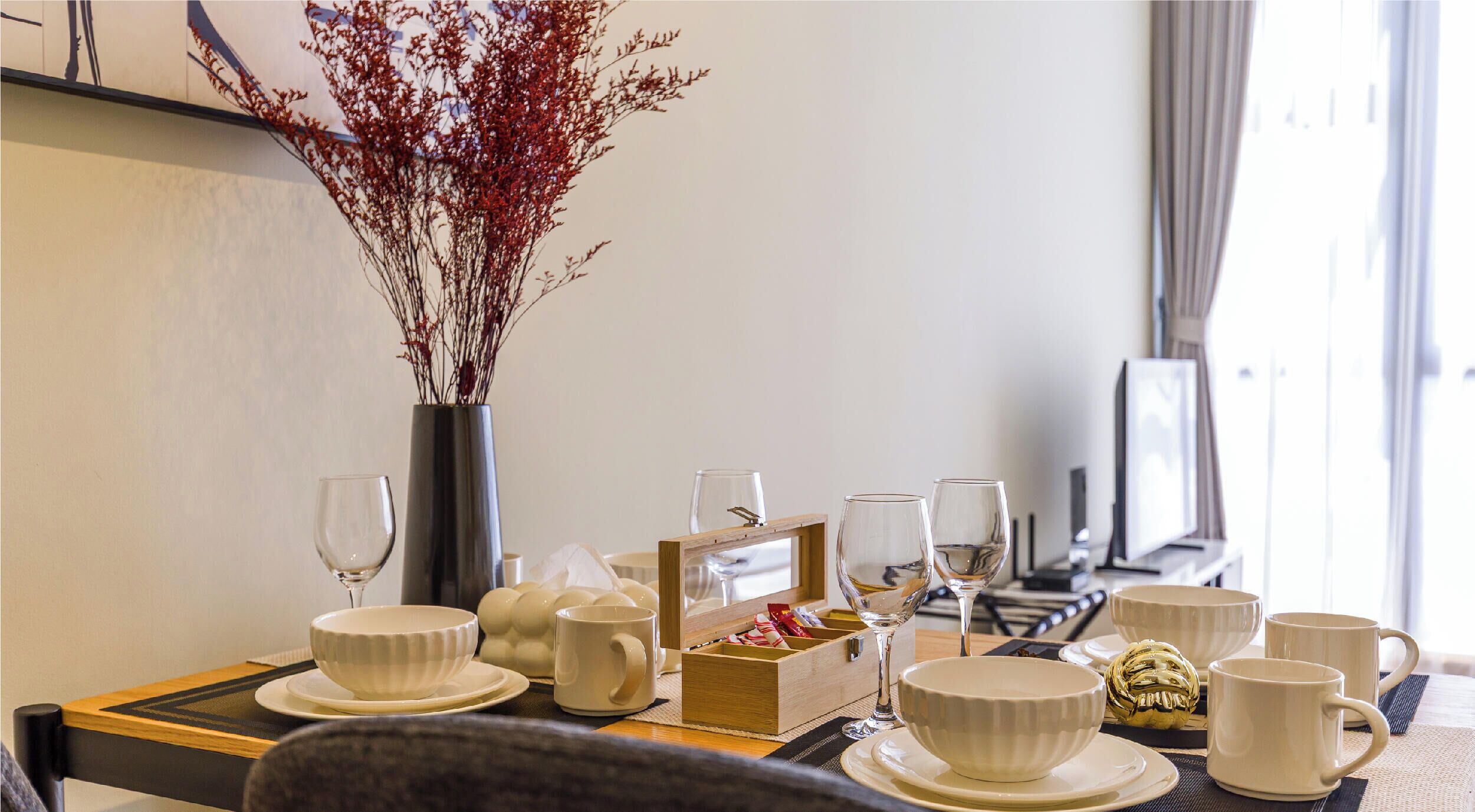 A dining table set with white ceramic bowls, cups, and a wooden box with snacks.