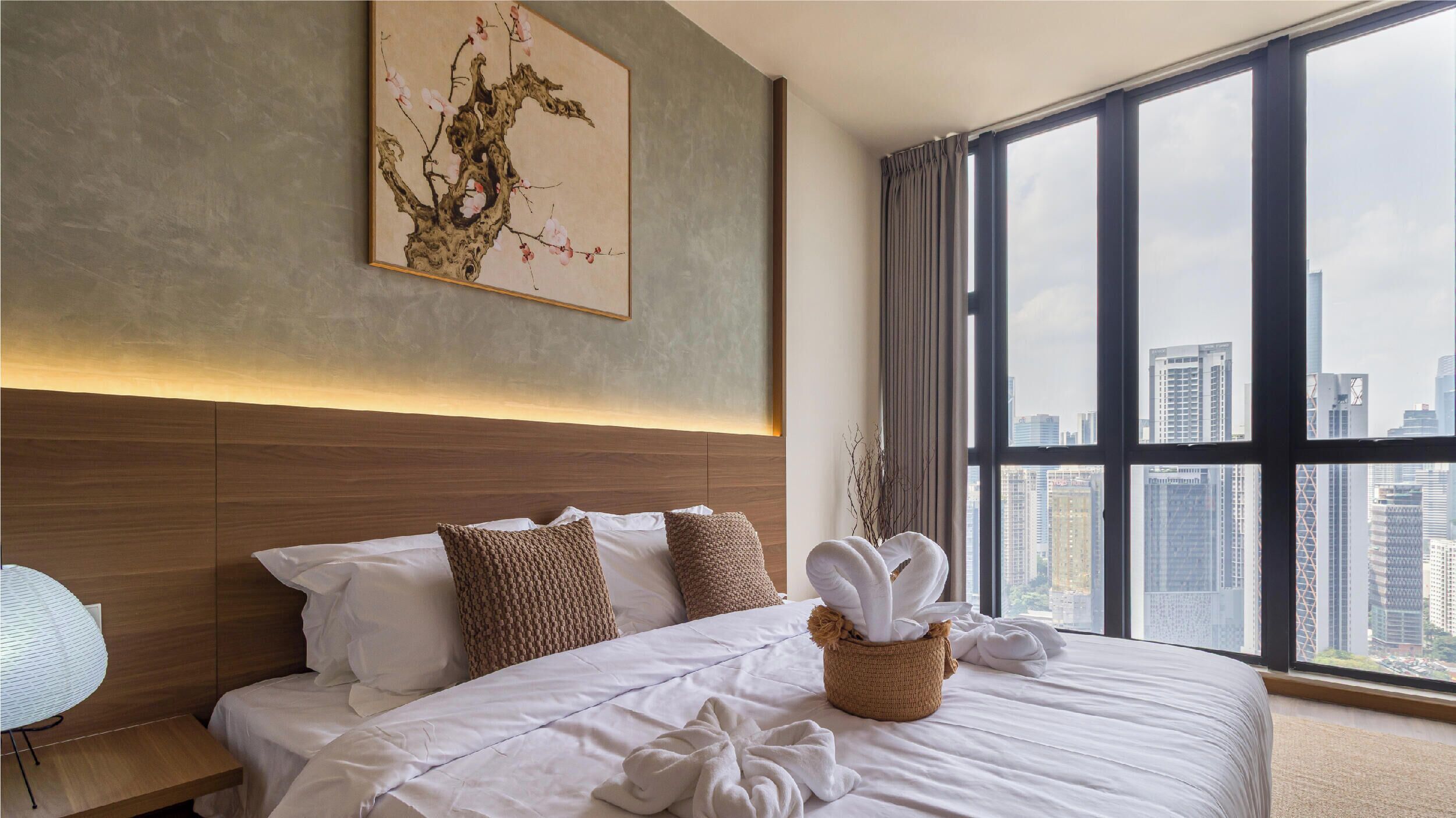 Una camera d'albergo con un letto grande, una testiera, vista sulla città attraverso ampie finestre e un'opera d'arte appesa al muro.