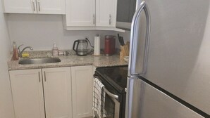 Une cuisine de taille réduite, dotée de meubles blancs, d’un réfrigérateur en acier inoxydable, d’un four à micro-ondes et d’une cuisinière.