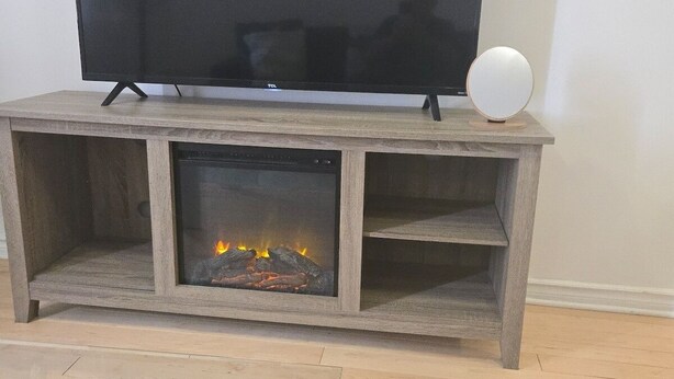 Un salon avec un téléviseur à écran plat posé sur un meuble en bois, une cheminée et une table basse en verre.