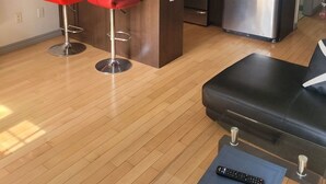 Una cucina moderna con pensili scuri in legno, un frigorifero in acciaio inossidabile, un forno a microonde e un piano cottura a gas. Sono presenti due sgabelli da bar rossi e un divano nero con un telecomando sopra.