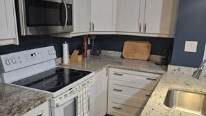 Een keuken met witte kastjes, een roestvrijstalen magnetron, een fornuis en een spoelbak.