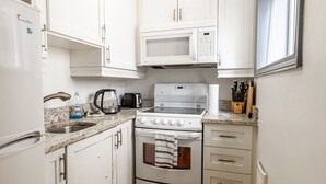 Una cocina compacta con gabinetes blancos, un microondas, una estufa y un lavamanos.