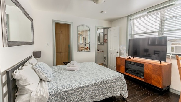 Ein Schlafzimmer mit Bett, Fernseher, Kommode und einem Fenster mit Jalousien.