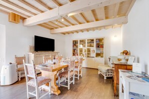 A spacious living area with a dining table set for four, a television mounted on the wall, and a bookshelf filled with books and decorative items. - Family Home Margherita Pool Mugello 6, Vicchio, Italy (Vicchio)
