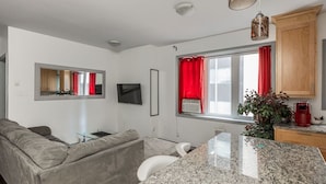 A modern living room with a grey sofa, a TV, and a kitchen area with granite countertops and red curtains. - Lovely App Downtown Ottawa 211D (Ottawa)