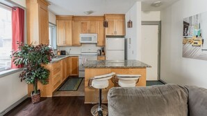 A compact kitchen with wooden cabinets, a microwave, a refrigerator, and a bar stool. - Lovely App Downtown Ottawa 211D (Ottawa)