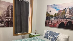 Een slaapkamer met een bed, een nachtkastje, een raam met gordijnen en twee wanddecoraties.