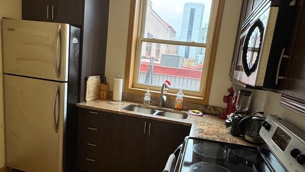 Een keuken met donkere kastjes, roestvrijstalen apparatuur, een granieten aanrechtblad en een raam met uitzicht op gebouwen.