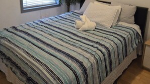 Ein Schlafzimmer mit einem Bett, einem Fenster mit Jalousien, einer Zimmerpflanze und einem Stadtbild.