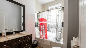 Ein Badezimmer mit einem großen Spiegel, einer dunklen Holzkommode, einem weißen Waschbecken, einer Badewanne und einem Fenster mit Vorhang in der Farbe eines Telefonhäuschens.