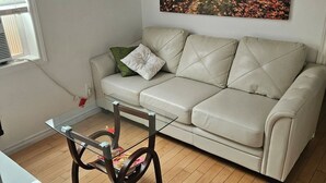 Ein Wohnzimmer mit einem beigen Sofa, einem Glastisch und einem Gemälde von einem Wald.