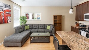 A modern living room with a sectional sofa, a coffee table, and a kitchen area with granite countertops and wooden cabinets. - 2-Bed App Downtown Ottawa 36D (Ottawa)