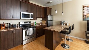 A modern kitchen with dark wood cabinets, stainless steel appliances, a granite countertop, and a bar area with stools. - 2-Bed App Downtown Ottawa 36D (Ottawa)