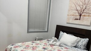 Een slaapkamer met een bed, een raam met zonwering, een radiator en een schilderij aan de muur.